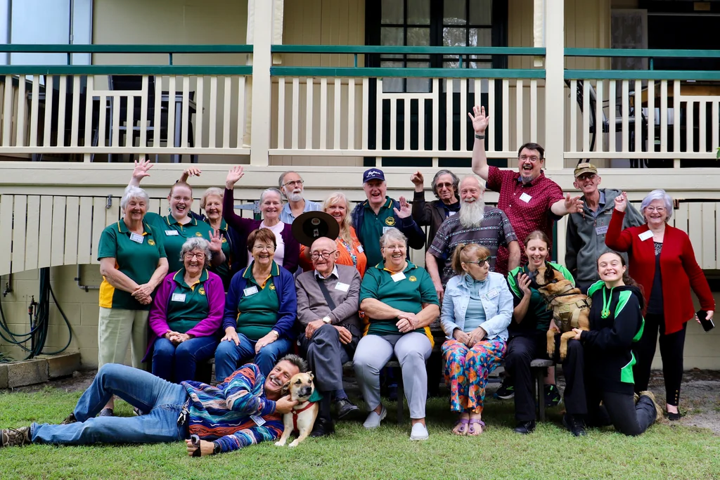 Toc H Queensland members gathered together on the grass in front of Coungeau House, waving and smiling for the group photograph